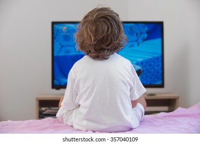 Little boy sitting on bed watching television.