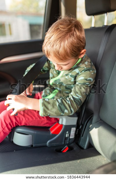 Little boy sitting on a\
booster seat trying to buckle up in the car. Children\'s Car Seat\
Safety