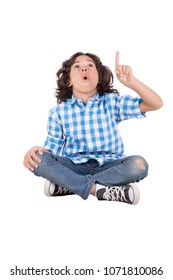 Little boy sitting on the floor crossed legs looking up and pointing with one finger, isolated on a white background.