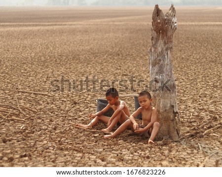 Little boy sitting on the ground near the tree stump dry of global warming
