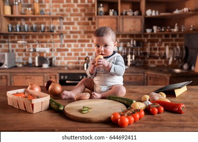 Little Boy Sitting On Kitchen Table Around Of Raw Vegetables Before Cooking A Dinner 