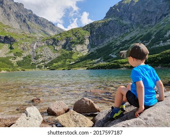 Little boy sitting on rocks with his back looking at the mountain lake, Velicke mountain lake, Slovakia, High Tatras
