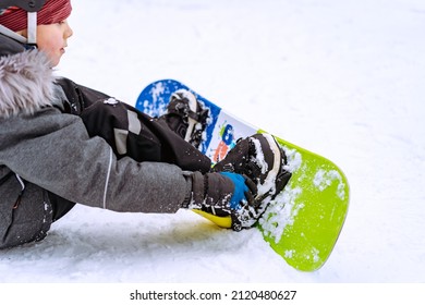 little boy sitting on snow putting his feet in snowboard bindings adjusting straps. High quality photo
