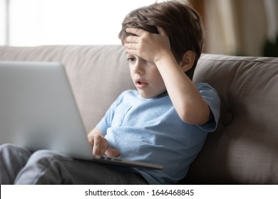 Little Boy Sitting On Sofa, Looking At Computer Screen, Shocked By Inappropriate Content, Parental Control Concept. Small Kid Reading Bad News, Feeling Stressed Or Worrying About Broken Device Virus.