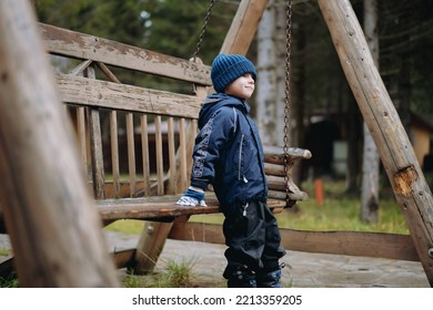 little boy sitting on solid wooden garden swings next in the countryside on autumn rainy day. High quality photo