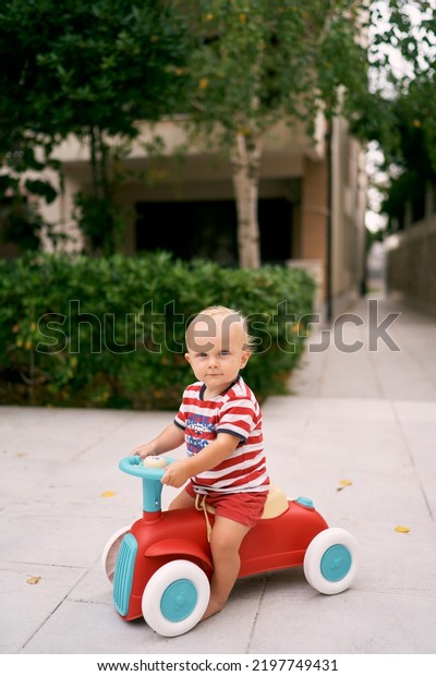 Little boy sitting on a toy car on a paved path in
the garden