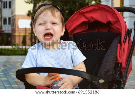 Little boy sitting in a pram and holding a drinking water bottle and capricious (crying)