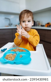 A little boy sitting at a table with a plate of food. A Curious Toddler Enjoying His Meal at the Table - Shutterstock ID 2395430981