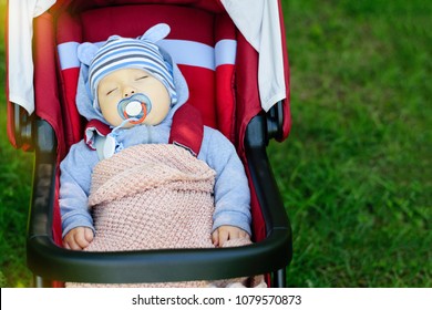 Little boy sleeping in red stroller in the park with a pacifier in mouth. Portrait of a child sleeping calmly in push chair outdoor with a dummy. Children day sleep and benefits for health concept