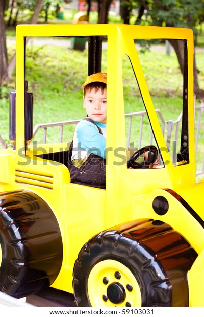 a little boy smiling and playing\
in the toy car in the children\'s village on a summer\
day
