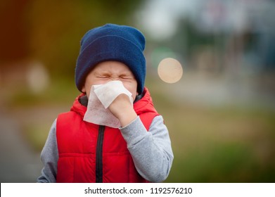 Little Boy Sneezing With Tissue Outdoors. Sick Child With Napkin In Autumn Park. Allergic Kid, Flu Season. Kid With Cold Rhinitis