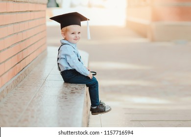 Little boy in spectacles and academic hat standing over against a brick wall of a school. Holds a magnifying glass and studies the environment - Powered by Shutterstock