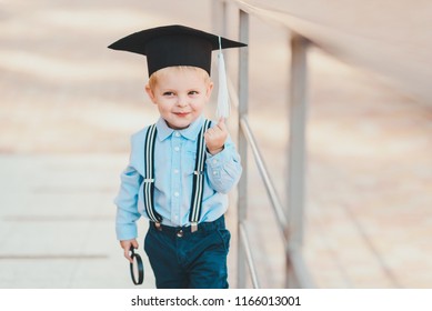 Little boy in spectacles and academic hat standing over against a brick wall of a school. Holds a magnifying glass and studies the environment - Powered by Shutterstock