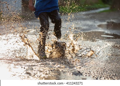 Little boy splashing in a mud puddle, jumping into a puddle
