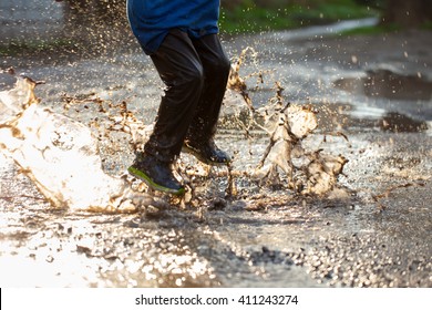 Little boy splashing in a mud puddle, jumping into a puddle
