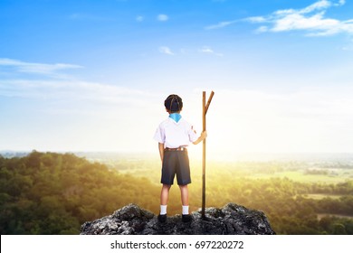 Little Boy Standing On Peaks And Looking At An Sun Light. Kid In The Scout Series Holding Pole And Begins The Adventure. Success, Leader And Winner Concept