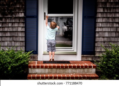 Little Boy Standing On Tip Toes Trying To Open Front Door Of House