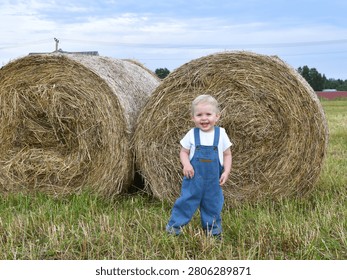 a little boy stands next to a haystack
