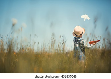 Little boy in straw hat is launching paper planes. One plane is white and the second is red. Back view. Image with selective focus and toning.