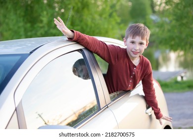 The Little Boy Stuck His Head Out Of The Car Window. The Child Sits In The Car And Looks Out The Window Glass