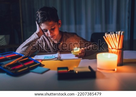 Little boy studying in low light with a burning candle.  Power outage, energy crisis concept.