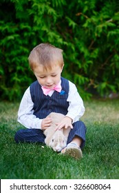 Little Boy In A Suit Playing In The Park With A Rabbit.