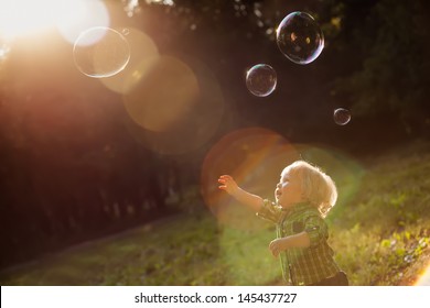 little boy in the sunset catches soap bubbles