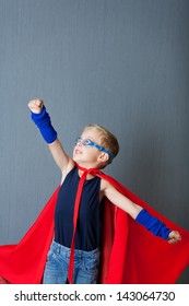 Little boy in super hero costume pretending to fly against blue wall