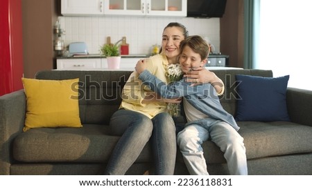 Little boy surprise his mother with a gift on Mother's Day. Happy family portrait. Little boy giving flowers to his mother at home as a birthday or mother's day gift.