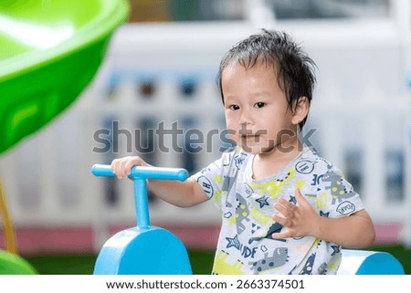 A little boy sweats profusely while playing on playground equipment at an outdoor playground on a hot day. Asian child, 2-3 years old.