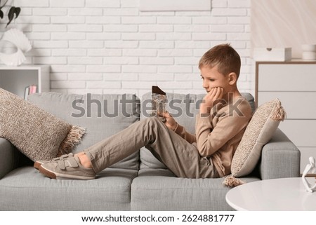 Little boy with sweet chocolate suffering from toothache at home