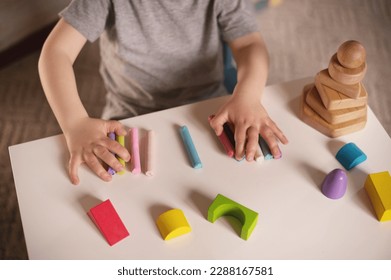 little boy three years old sits at  table with colored crayons and plasticine and plays sensory educational games. Closeup of hands focus on colored plasticine and constructor. Unrecognizable no face
