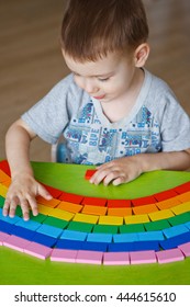 Little Boy (three Years Old) Puts A Rainbow Of Dominoes. The Development Of Color In Preschool Child. A Child Plays With Eco-friendly Wooden Toys