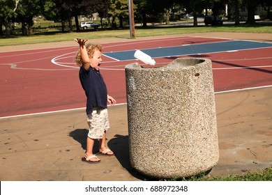 A Little Boy Throwing Away His Milk Cartoon In A Public Trash Container At The Park. The Child Is Cleaning Up The Playground From Trash And Debris.  Don't Litter Concept. 