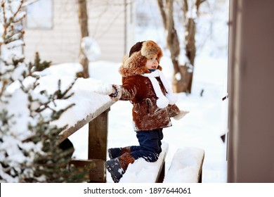 A Little Boy Throws A Snowball Through The Window While Sitting On A Snow Covered Bench