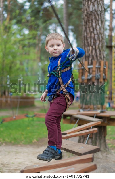 A little boy is training in a rope park. The child\
climbs the obstacle course. Active recreation in the park in the\
fresh air.