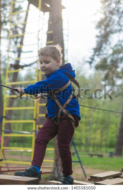 A little boy is training in a rope park. The child\
climbs the obstacle course. Active recreation in the park in the\
fresh air.