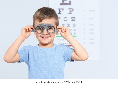 Little boy with trial frame near eye chart in hospital, space for text. Visiting children's doctor
