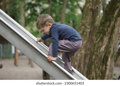 Little Boy trying to going up the slider. Preschool child playing on outdoor playground. Happy toddler child climbing and having fun with summer outdoors activity - Powered by Shutterstock