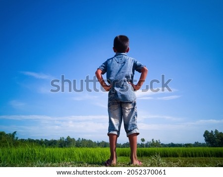 Little Boy Under Clear Autumn Sky. Man Enjoying The Beauty Of Autumn Sky. Man With Blue Sky Clouds In Bangladesh With Selective Focus. Copy Space. Blurry Rice Field Background. 