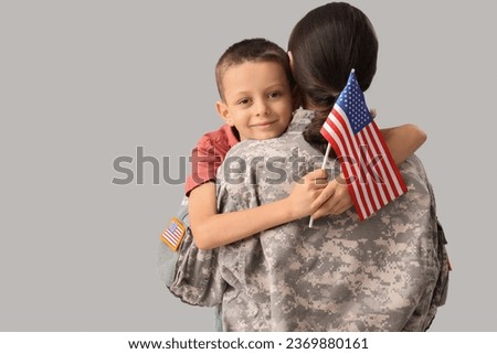 Little boy with USA flag hugging his military mother on light background. Veterans Day celebration