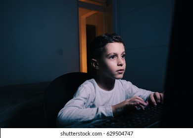 Little Boy Using Computer At Night In Bedroom