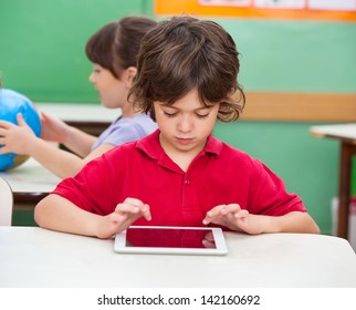 Little boy using digital tablet at desk in classroom