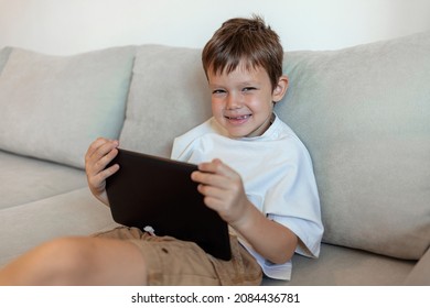 Little boy using digital tablet on bed during the day. Growing up in a technology-based world. Shot of a young boy using his digital tablet while lying on the sofa, looking at camera and smiling. - Powered by Shutterstock