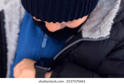 little boy using smartwatch from hand sitting outside, talking on device. kid dressed in autumn cap and scarf and warm jacket.smiling child with one teeth missing.close up  - Powered by Shutterstock