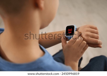 Little boy using SOS function on smartwatch indoors, closeup