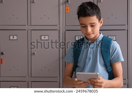 Little boy using tablet computer near locker at school