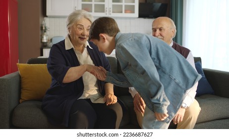 The little boy visited his grandfather and celebrated Eid al-Fitr by kissing their hands. Happy senior couple sitting on sofa kissing and hugging their little grandchild.  - Shutterstock ID 2236687627