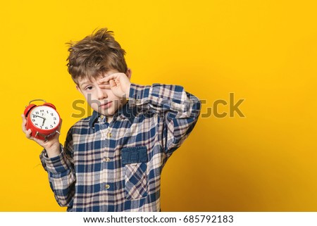 Little boy waking up with alarm clock, isolated on the yellow background.
