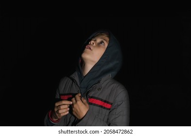 A little boy in warm clothes with a hood looks at the sky in the dark